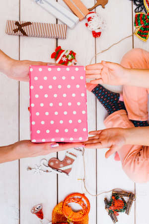 Christmas teamwork. Festive family help. Unrecognizable females wrapping gifts on wooden background top view, beauty tinsel. Presents decoration processの写真素材