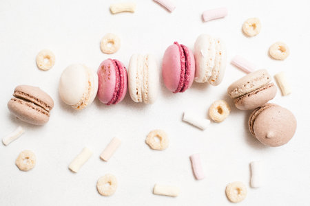 Sweet culinary art of macaroons on white backdrop, top view. Delicious cakes with corn flakes and...