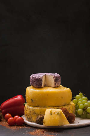 Gourmet sorts of cheese with variety of vegetables, fruits and spices on black background. Assortment composition of luxury products, close up, free space. Rustic local dairy advertisementの写真素材