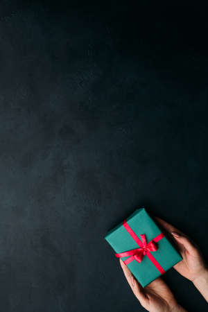 presenting an elegant gift on dark background. closed gift box wrapped with ribbon and a bow. pleasant surprise for birthday, new year, christmas, valentines day and other holidays.の写真素材