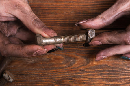 Female dirty hands holding a screw nut and a bolt on a wooden background. Dirty job is not a problem...