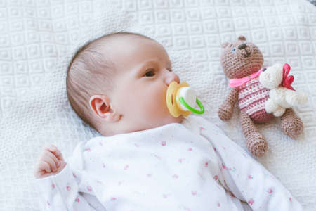 newborn baby laying on bed with his own toy bear. mothers treasure. beginning of lifeの写真素材