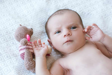 newborn baby laying on bed with his own toy bear. mothers treasure. beginning of lifeの写真素材