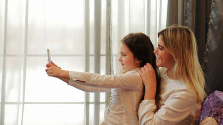 happy family. mother daughter leisure moments. fun pastime. young mom and kid posing for selfie at homeの写真素材