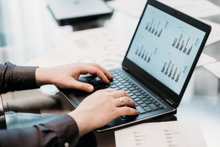 Business paperwork. unrecognizable man typing on laptop. graph documents on the screen