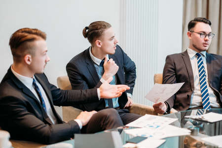 lively discussion and communication on business meeting. three young managers talking about company dealings. men in office workspaceの写真素材