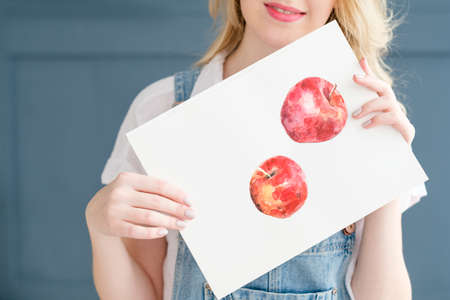 creative leisure. painting hobby. artful personality. talented girl holding her watercolor drawing of applesの写真素材