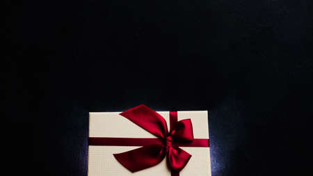 luxury stylish present on dark background. soft cream gift box with ruby red ribbon bow. elegant and exclusive reward on birthday or valentines day. free space conceptの写真素材