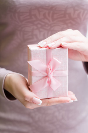 woman holding a present in a box. beautiful tender soft pink package with a bow. holiday gift for a...