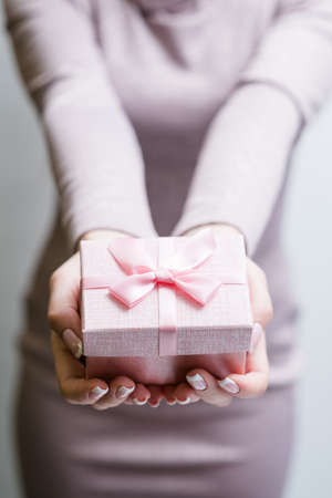 woman holding a present in a gift box. perfect reward for celebration of birthday or anniversary. soft pink package with a bow.の写真素材