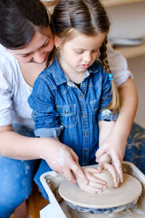 family artistic leisure. pottery hobby and handicraft pastime. mother and daughter working on potter wheel together.の写真素材