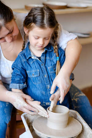 pottery workshop. handmade craft. artisan teaching a child girl how to form and shape clay on potter wheelの写真素材