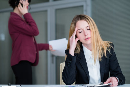 headache and fatigue concept. tired woman rubbing her temple. office workspace and business...