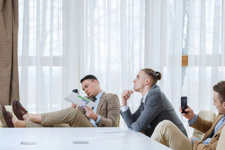 bored indifferent business men on board meeting. waiting for boss. idlers at work killing timeの写真素材