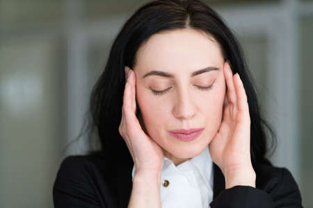 headache stress tiredness concept. woman massaging her temples. face portrait of young business brunette ladyの写真素材