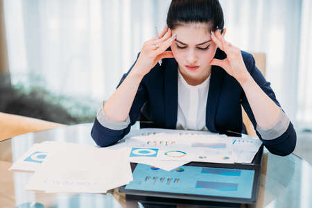 headache from work overload. stress and fatigue concept. young beautiful business woman sitting in office reading documents and papersの写真素材