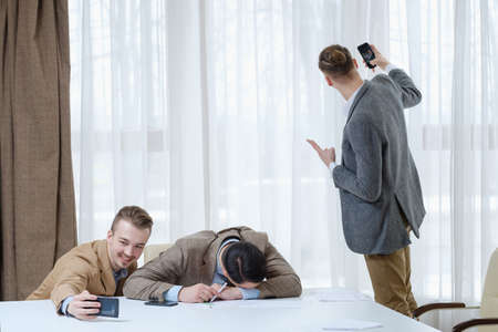 office jokes and fun. friendship and comradery at work. business men taking selfie with a sleeping tired colleague.の写真素材