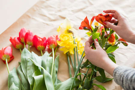 florist at work. woman hands arranging a spring flower bouquet from assortment of alstroemeria red tulips and narcissusの写真素材