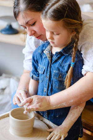 family artistic leisure. pottery hobby and handicraft pastime. mother and daughter working on potter wheel together.の写真素材