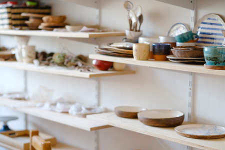 pottery business. handicraft handmade production. assortment of craft crockery and clay plates on shelves in workshopの写真素材