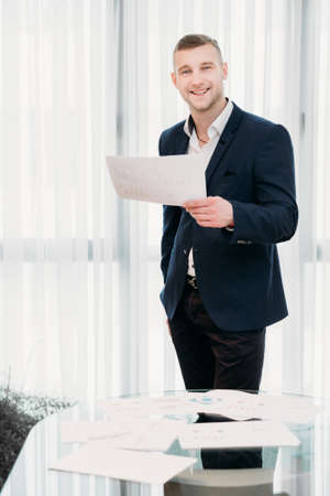 corporate manager. company ceo. profession job concept. young handsome successful business man standing in light office holding papers.の写真素材