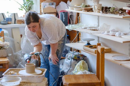 pottery workshop interior. clay dishes collection and assortment on shelves. potter in process of...