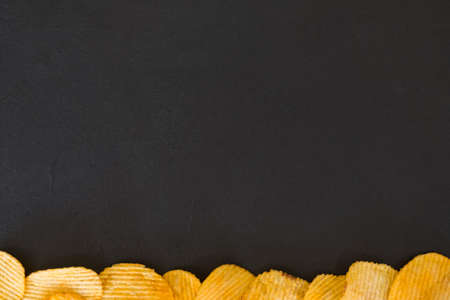 chips food background. wavy ridged potato crisps in the bottom of dark background. salty spicy crunchy slicesの写真素材