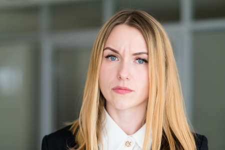 emotion face. woman with a quizzical interrogatory inquiring look. business lady at office workspace. young beautiful blond girl portraitの写真素材