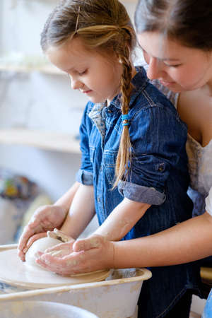 handmade hobby pottery courses. master class at workshop. potter forming clay on turning wheel with a little student girlの写真素材