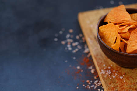 tortilla nacho chips food on dark background. salty spicy crunchy slices in a bowl on a cutting board. copyspace conceptの写真素材