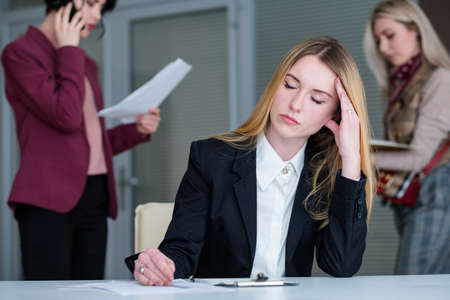 headache and fatigue concept. tired woman rubbing her temple. office workspace and tiring business lifestyleの写真素材