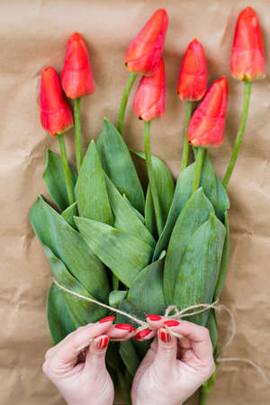 floristry art. florist making a bouquet of red tulips. simple and beautiful spring flower arranging.の写真素材