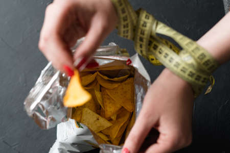 diet eating vs fast food. woman hands tied with measure tape. forbidden chips snack. healthy lifestyle choicesの写真素材