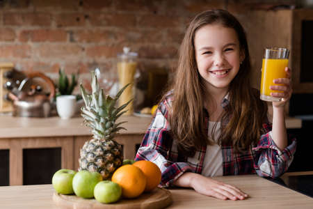 child healthy food and balanced nutrition. fresh orange juice and fruit breakfast. smiling little girl in the kitchen ready to have a wholesome morning mealの写真素材