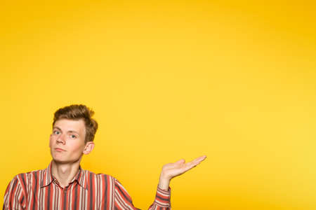 handsome young man pointing sideways with hand as if showing to smth. portrait of a guy on yellow background. copyspace for advertisement.の写真素材