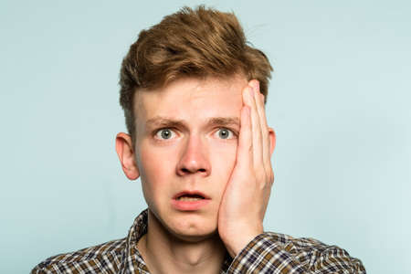 scared shocked terrified frightened startled man clutching hands to his face. portrait of a young guy on light background. emotion facial expression. feelings and people reaction concept.の写真素材