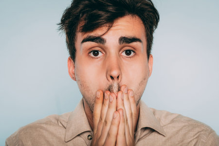 regret and remorse. sad distraught man covering mouth with hand. portrait of a young brunet guy on...