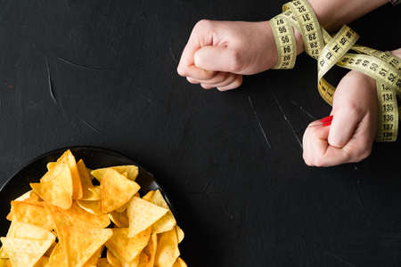 healthy diet eating. weightloss and fit body. woman hands tied with measuring tape. no chips today.の写真素材