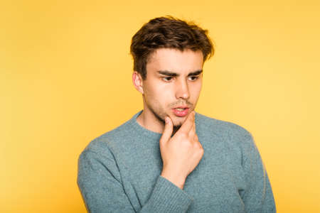 Puzzled bewildered man thinking over something or contemplating. scratching his beard. portrait of a young brunet guy on yellow background. emotion facial expression. feelings and people reaction concept.の写真素材