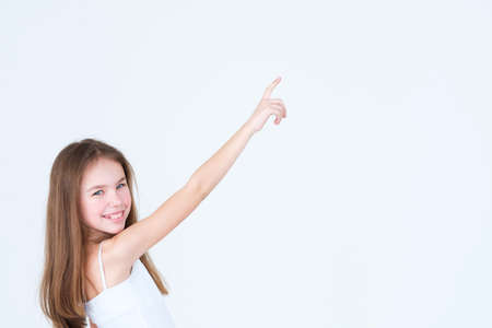 Cute little girl pointing to something with a hand and index finger. portrait on white background. advertisement and free space concept.の写真素材
