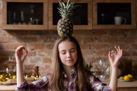 balanced nutrition and healthy eating for children. organic fruit for health wellness and fitness of youngsters. girl holding a pineapple on her headの写真素材