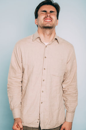 man face disturbed with pain grimace. unbearable suffering and torture. portrait of a young brunet guy on light background. emotion facial expression. feelings and people reaction concept.の写真素材