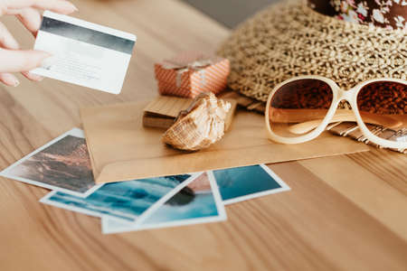 money loan for summer vacation. holidays traveling and resort destinations concept. woman holding a credit bank card. sun hat sunglasses and seaside photos on the desk.の写真素材
