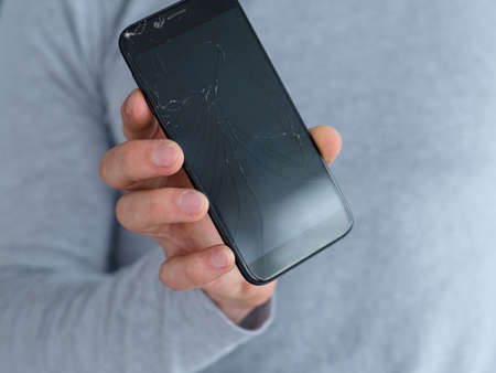 smashed shattered cracked screen. man holding damaged smart phone. mobile devices repair service concept.の写真素材