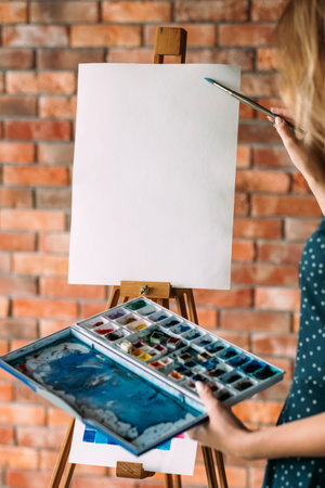 art therapy. painting classes or courses. creativity inspiration expression concept. blank paper on easel. woman holding a  palette. empty space for advertising.の写真素材