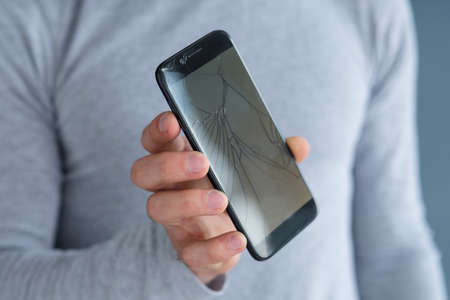 smashed shattered cracked screen. man holding damaged smart phone. mobile devices repair service concept.の写真素材