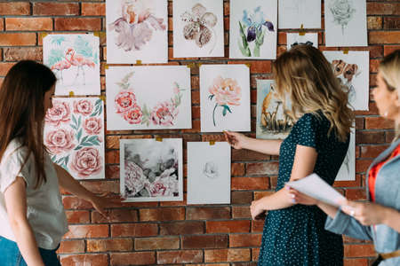 painting courses artwork. creative workshop decor. painting hobby and leisure concept. beautiful watercolor pictures of flowers and animals on the wall. students looking at drawingsの写真素材