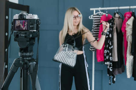 fashion stylist vlogging. social media influencer creating content. video streaming. woman showing a bag standing in clothing showroomの写真素材