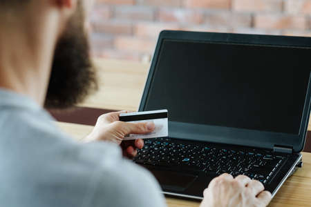 online shopping. man buying goods on the internet using his credit or debit bank card. empty laptop screen for e-commerce and free space concept.の写真素材