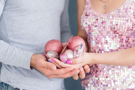 family christmas home decoration traditions. man and woman holding rose gold glittery balls and toys in hands. holiday festive ornament concept.の写真素材